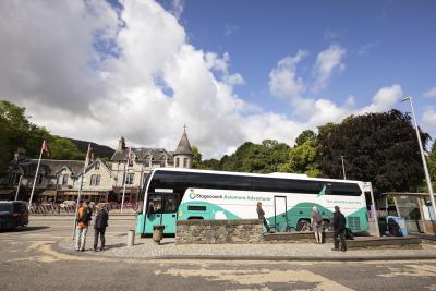 View of a street with the Aviemore Adventurer bus stopped at a bus shelter and hotel in the background.