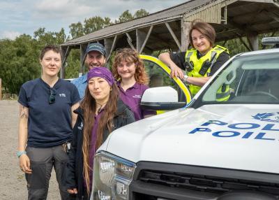 Five people (countryside rangers and a pollice officer) standing next to a police car with a shed in the background