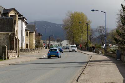 A street with a blue car and dark mountains in the background.