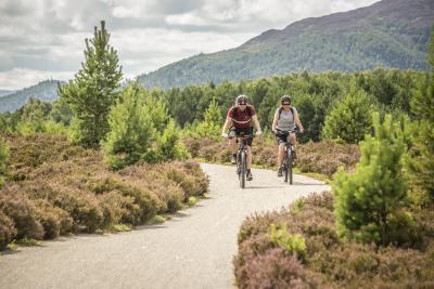 Two cyclists on the Speyside Way path with trees and heather on either side.
