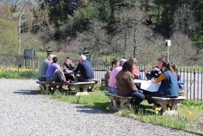 Two groups of people sit outside in the sun talking to one another