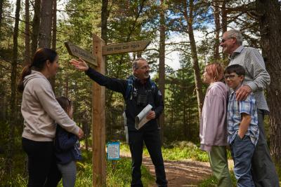 Forest scene with a countryside ranger in the centre of the picture pointing directions out for a family.