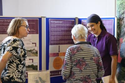 Three people having a conversation in front of information boards.