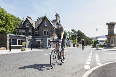 Person riding a bike down the street with another cyclist in the background.