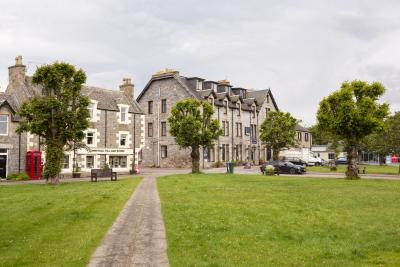 A view along a path in the village green with the Tomintoul village shop and a hotel in the background