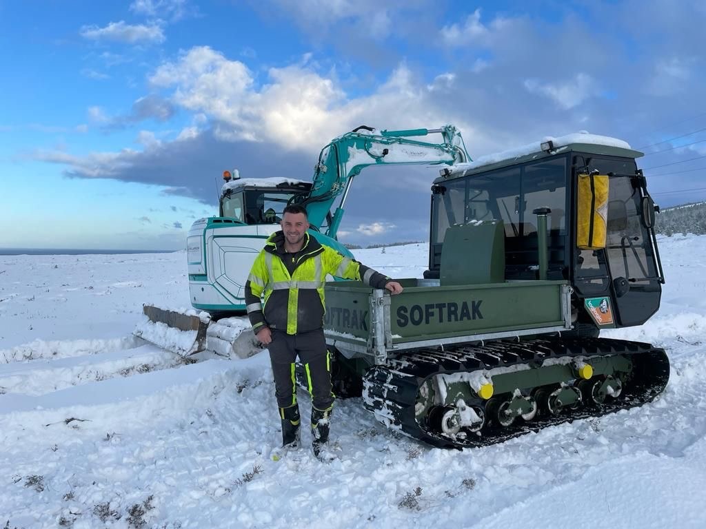 Image of Sean Williamson, wearing hi vis PPE equipment, standing beside machinery with snow on the ground.